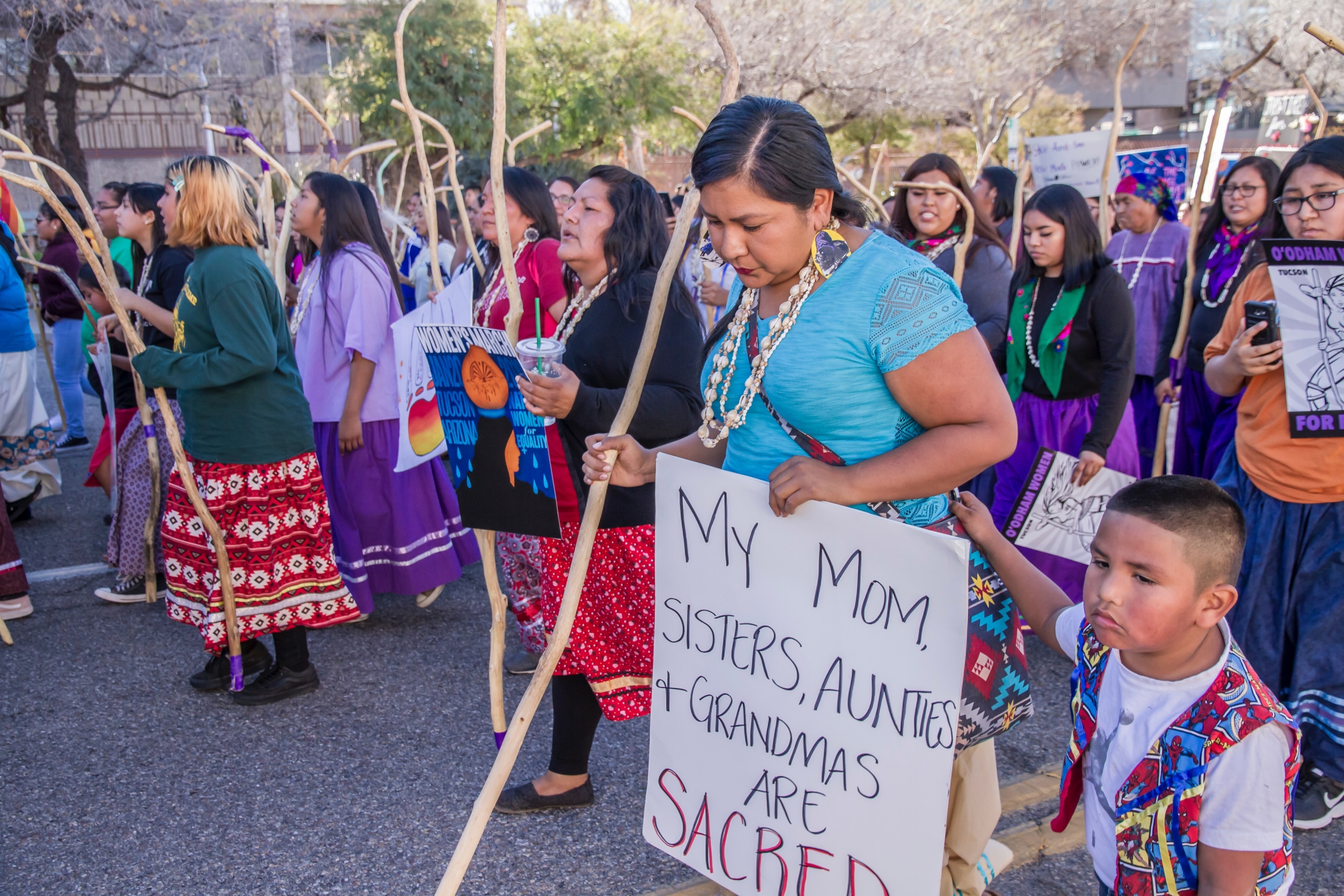 Group of indigenous women and children walking. Person towards front is holding a sign that reads "my mom, sisters, aunties, and grandmas are sacred."